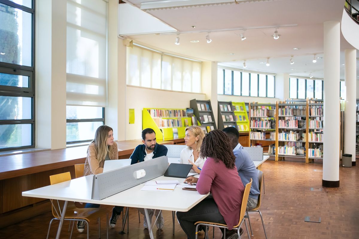 University students collaborating around a laptop during a library study session.